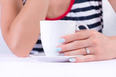 Güzel el elmas alyans ve mavi çivi lehçe manikür holding fincan kahve ve bulanık denizci ile t-shirt arka planda. Yaz ve tatil kavramı. Yakın, seçici odak