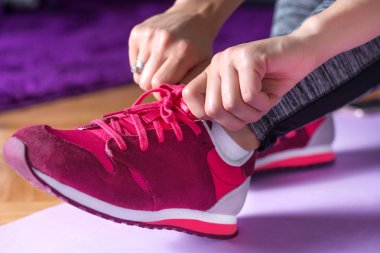 Genç kız bacaklarını hazırlama kırmızı spor ayakkabılar ile evde mor yoga ya da fitness mat üzerinde halledin. Spor ve rekreasyon kavramı. Yakın, seçici odak