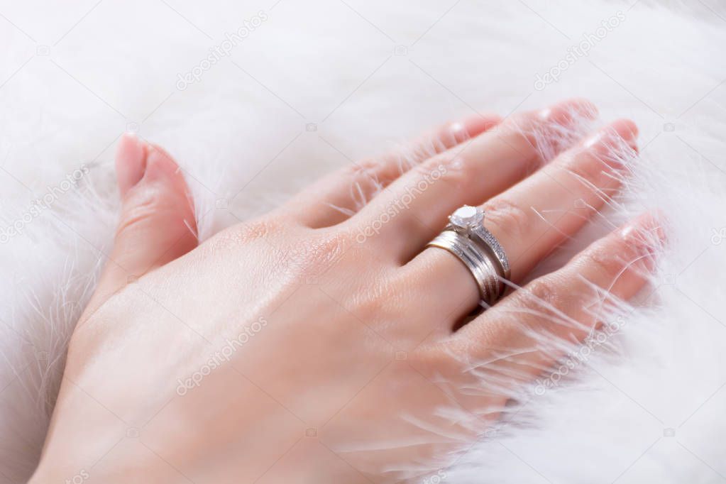 Young girl hands with diamond engagement ring on finger on white fur background. Fashion and beauty concept. Close up, selective focus
