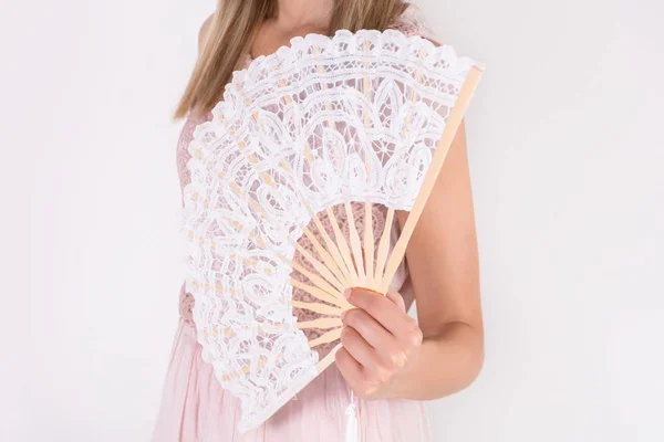 Beautiful young female in cream dress holding white lace hand fan isolated on white background. Summer and heat concept. Close up, selective focus