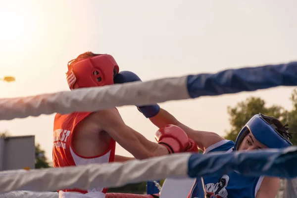 Nis, Serbia - August 14, 2018: Two mans boxing on match outdoor in ring at sunset. Fighters with protective gloves and equipment. Close up, selective focus