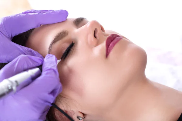 Dövmeci profesyonel salon güzel genç kız üzerinde kalıcı makyaj ile göz kalemi uyduruyor. Güzellik uzmanı yapım dövme makyaj mor eldivenler ve araçları ile. Yakın, seçici odak