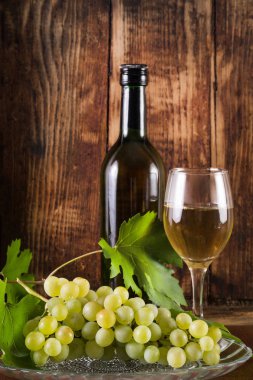 Tablo yeşil üzüm ve cam ve siyah şişe beyaz şarap asma ile dekore edilmiştir. Retro ve vintage ahşap arka plan. Yiyecek ve içecek dekorasyon konsepti. Yakın, seçici odak