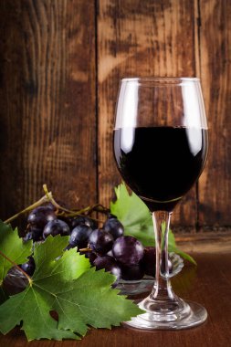 Kırmızı şarap cam ve üzüm asma dekorasyonu ile plaka üzerinde. Ahşap retro kahverengi zemin ve resepsiyon. Vintage yiyecek ve içecek konsepti. Yakın, seçici odak