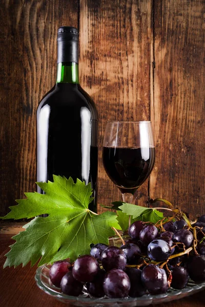 Kırmızı üzüm asma dekorasyon ve cam ve ahşap kahverengi retro masa üzerinde kırmızı şarap ile plaka üzerinde. Vintage yiyecek ve içecek konsepti. Yakın, seçici odak