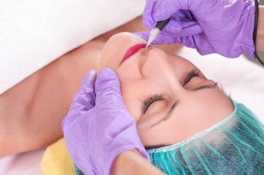 Kalıcı makyaj güzellik salonda dudaklarında sahip genç güzel kız. Dövme ile profesyonel ve steril alet uygulama güzellik uzmanı. Yakın, seçici odak