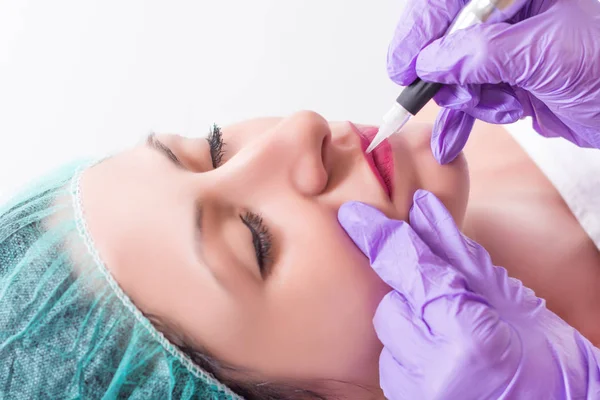 Kalıcı olan genç güzel kadın makyaj profesyonel güzellik salonda dudaklarında. Modern ve yeni araçlar ile dövme. Yakın, seçici odak