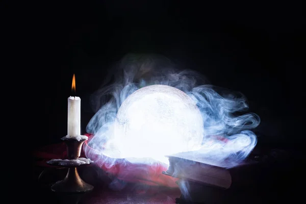 Kristal top Sihirbazı ve fortune teller sigara ve ışıklar tablo ve mum Şamdan ve eski kitaplar, siyah arka plan için. Cadılar Bayramı kavramı. Yakın, seçici odak