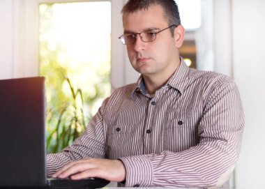 Dizüstü bilgisayar, danışmanı Avukat kavramı ile ofisinde çalışan iş adam. Modern gömlek ve gözlük ve klavyede yazarak..... .adam kullanıyor. Bulanık windows arka planda gün batımı ile. Yakın, seçici odak