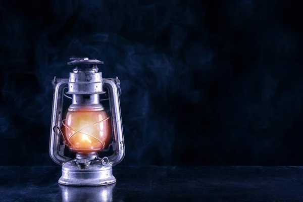 Old gas lamp on black table and foggy and smoke dark and night scenery background. Oil lantern burning at black background and empty space on right side. Horror and Halloween concept. Selective focus