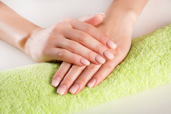 Woman hands with ombre french nails manicure on green towel in beauty studio. Manicure and beauty concept