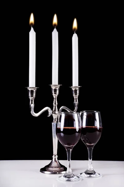 Baroque candlestick and two red wine glasses on white desk and black background. Romantic and stylish diner concept. Close up