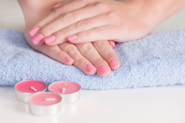 Yavaşça pembe jel kadın ellerinde mavi havlu ve resepsiyon Studio pembe mum Lehçe çivi. Manikür ve güzellik kavramı. Yakın, seçici odak