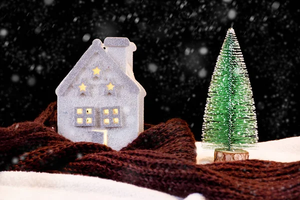 House and warming scarf around and green Christmas tree in night winter season. Snowflakes snowing in the scene. Winter idyll concept