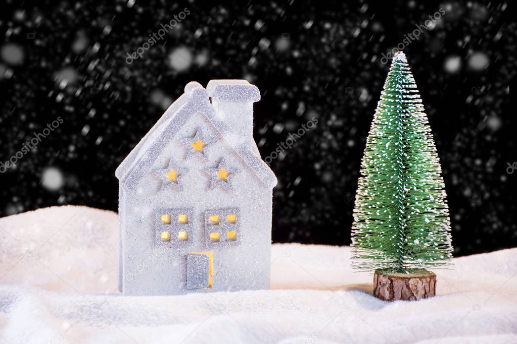 Small Christmas toy house and fir tree on snowing night with snowflakes. Winter season scene and idyll concept