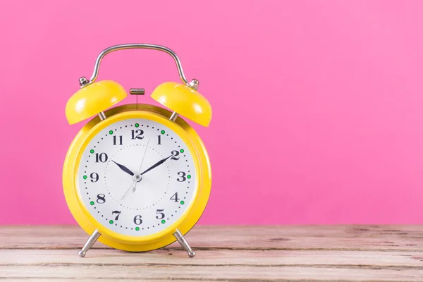 木製の机とピンクの女らしさの背景に時計のアラーム 時計は黄色と警報ベル テキストやデザインのためのスペース 時間の概念 — ストック写真
