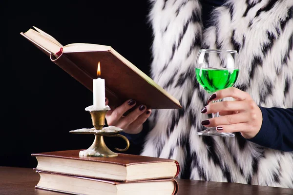 アブサン グリーンを持つ女性は 本を読んでガラスで飲みます 燃焼の机の上の燭台にキャンドルします 神秘的で魔法のコンセプト イメージ — ストック写真