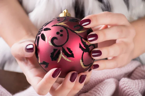 Kırmızı şarap rengi kızla Lehçe jel ve Noel top dekorasyon elinde tutan çiviler. Kış ve tatil kavramı manikür. Yakın, seçici odak