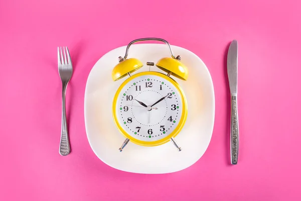 Tabak çatal ve bıçak, pembe arka plan izole Retro çalar saat. Chrono beslenme diyet kavramı. Üstten görünüm