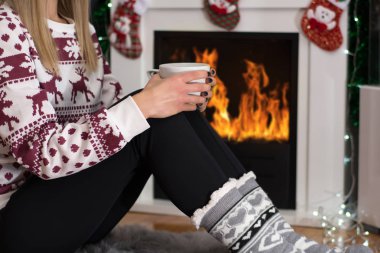 Çay ayağı üzerinde tutan ve uzun kış geceleri evde şömine ateşte ısınma kız. Kadın yün kazak, çorap giyer. Kış ve soğuk hava kavramı. Yakın, seçici odak