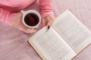 Fincan çay ve kitap ile üstten görünüm bir kız. Kitap okuma Pembe Yün kazaklı kadın. Eğitim ve soğuk hava kavramı. Yakın, seçici odak