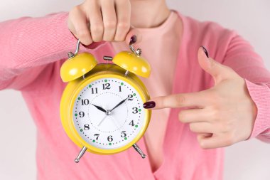 Genç kadın retro eski ile alarm saati el ve parmak ile zamanında gösterir. Sarı renk pembe kazak ve saat kızıdır. Zaman kavramı görüntü. Yakın, seçici odak