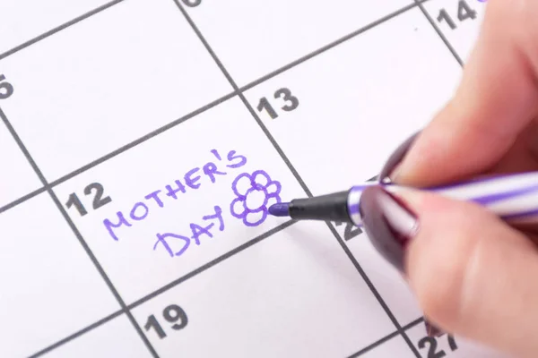 Woman hand writing Mothers Day and drawing flower with purple felt pen in calendar. Mothers day holiday concept. Close up, selective focus