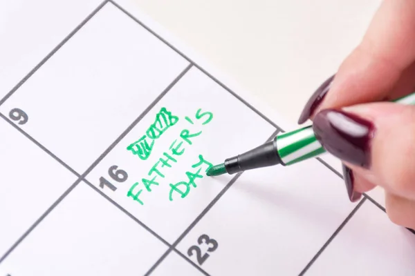 Woman hands with green felt pen writing words Fathers Day and drawing tie bow in calendar. Fathers Day holiday concept. Close up, selective focus