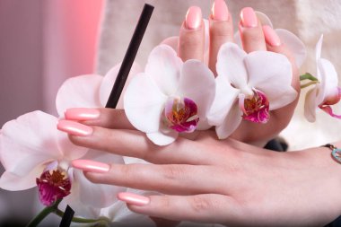 Young woman hands with pink spring manicure on nails holding white orchids flower in hands in beauty salon. Manicure and Beauty concept. Close up, selective focus clipart