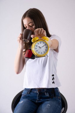 Elinde retro saati olan genç bir kız zamanı gösteriyor ve beyaz arka planda izole edilmiş kahve içiyor. Kadın bulanık. Yaklaş, seçici odaklanma