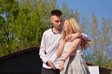 Nis, Sırbistan - 20 Nisan 2019, Genç sarışın kız ve adam arka planda yeşil bir ağaç ile parkta güneşli bir bahar gününde sarıldı. Yakın çekim, seçici odak. Aşk ve tutku çift kavramı