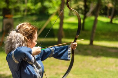 Niş, Sırbistan - 16 Haziran. 2019: Geleneksel bir takım elbiseyle şövalye festivalinde ormanda ok ok atan kadın okçu. Bowman longbow çekim den önce. Yakın çekim, seçici odak