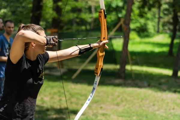 Nis, Serbia - June 16. 2019: Professional girl archer with bow shoot arrow in the forest on knight festival and tournament. Bowman before shooting from a longbow. Close up, selective focus