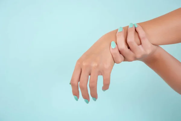 Woman hands with turquoise color nails polish in beauty studio isolated on blue soft blue background. Manicure and beauty concept. Close up, selective focus