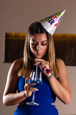 Gece kulübünde mavi lagün kokteyli içen başında doğum günü şapkası olan güzel bir kız. Doğum günü partisi konsepti. Yakın çekim, seçici odak