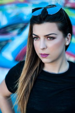 Güzel bir kız, kafasında gözlüklerle bir bahar günü renkli bir duvarın önünde poz veriyor.