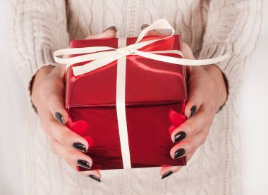 İçinde yay olan hediye kutusu siyah tırnaklı ve kazaklı genç kadın eli, yakın çekim.