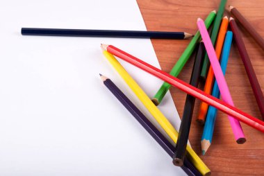 Beyaz kağıda dökülen renkli kalemler ve ahşap masa, kapat.