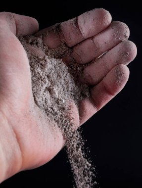 Siyaha izole edilmiş insan elinden gri kül dökülüyor. Kapatın. Seçici odak