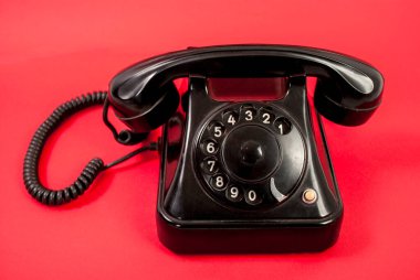 Kırmızı arka planda izole edilmiş eski siyah telefon