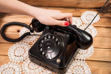 Dantel masa örtüleri ve ahşap arka planda eski telefon kulaklığı tutan bir kız.