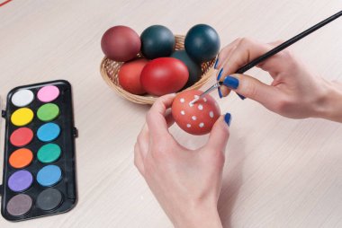 Kız elleri tahta masada fırçayla Paskalya yumurtası boyuyor. Kapat.