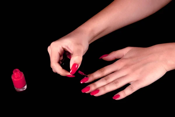 Girl applying red nail polish isolated on black background