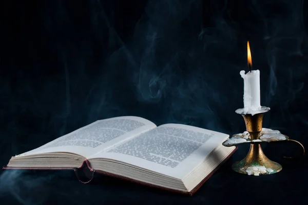 古いオープンブックとキャンドルで燭台と煙で暗い黒の背景 — ストック写真
