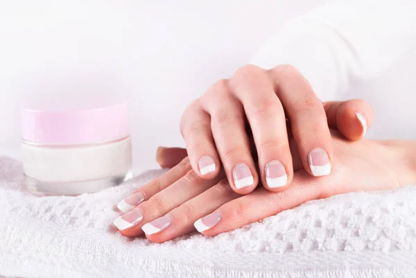 Woman hands with french manicure and pink hand cream on white towel
