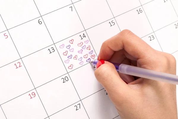 Woman hand with pencil drawing hearts shape in calendar for Valentines day