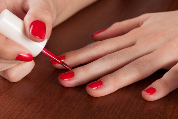 Girl paint nails with red nail polish on wooden table. Close up