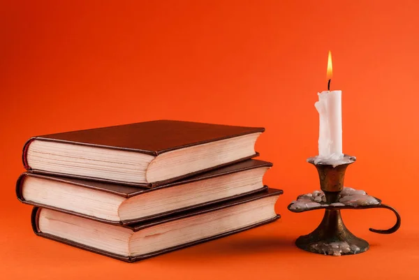 Свеча Горит Подсвечнике Три Старые Книги Изолированы Оранжевом Фоне — стоковое фото