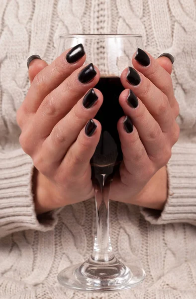 Young female hands with black nails and sweater holding wine glass, close up