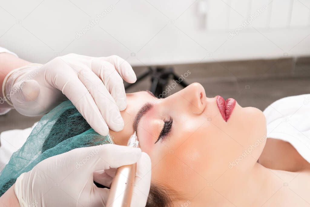 Close up of cosmetologist applying permanent make up on female eyebrows. Permanent make up tattoo